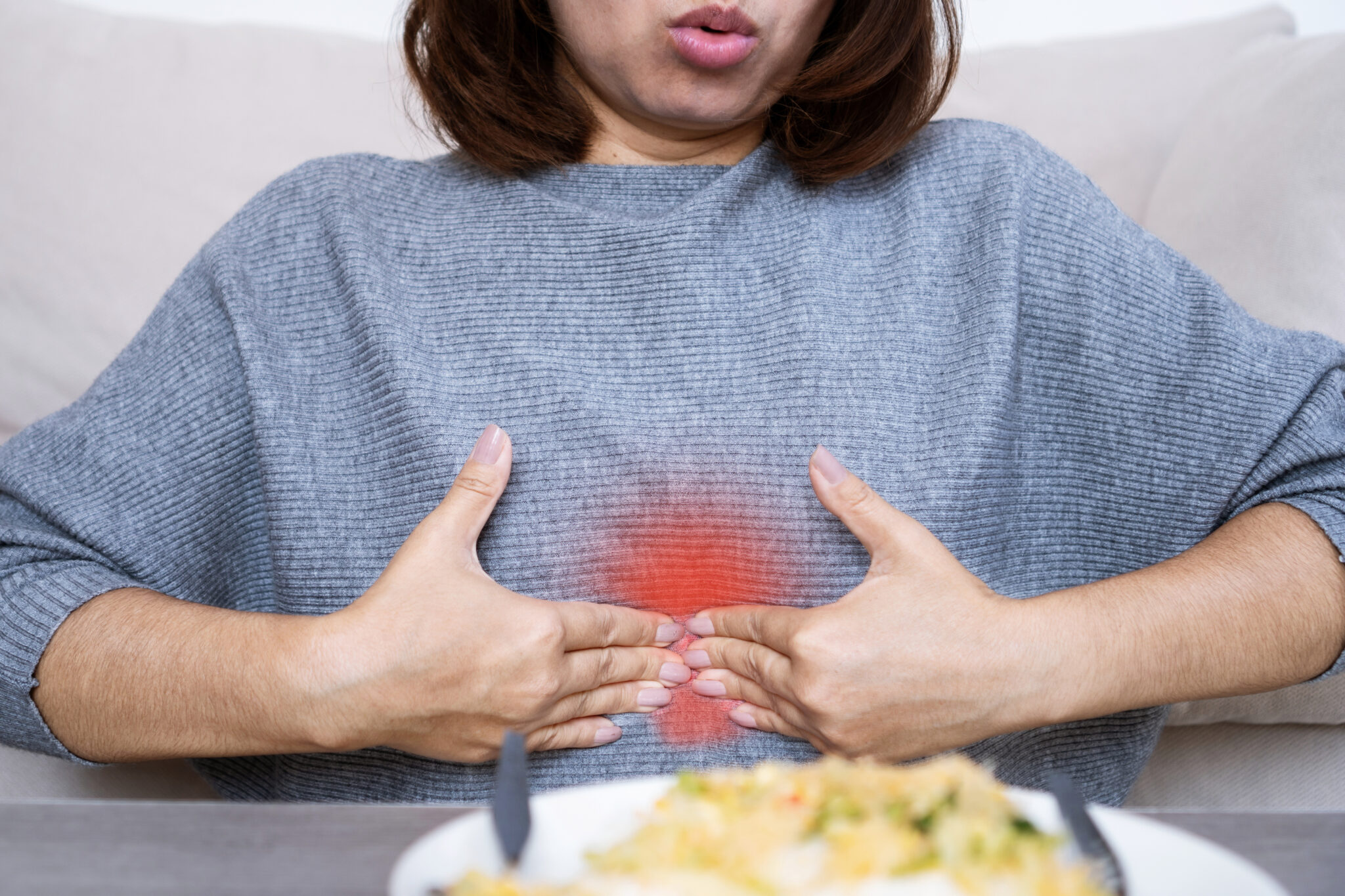 Asian woman suffering from epigastric burning and pain due to dyspepsia and acid reflux, feeling discomfort in upper abdomen after eating food
